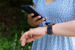 Woman with smartphone and smartwatch on hand in summer park. Using apps for notifications, hiking and sports training