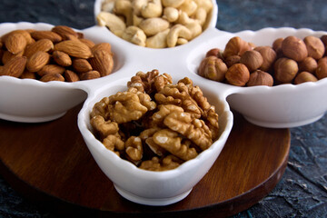 Wall Mural - Assorted hazelnuts, cashews, almonds and walnuts on a white platter on a wooden stand. A variety of healthy nuts for snacking and healthy nutrition