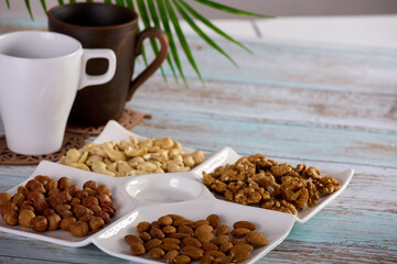 Wall Mural - Assorted nuts are laid out on a square-shaped plate along with empty glasses for hot drinks. Dried nuts of various types are beautifully placed on a square menagerie standing on a wooden table