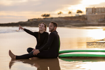 Wall Mural - Happy Young Couple Relaxing On The Beach After Surfing Day