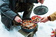 © Andrew Kornylak - A man serves hot venison stew onto a dish from a cast iron pot in the snow