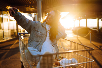 Wall Mural - Selfie time. Young woman having fun on shopping trolleys. Black friday. Consumerism, sale, discounts, lifestyle concept.