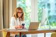 © sepy - Confident mid aged businesswoman sitting at desk and using mobile phone in her luxury office