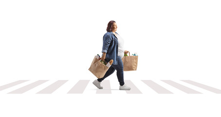 Wall Mural - Corpulent woman with grocery bags crossing a street and walking at a pedestrian crosswalk