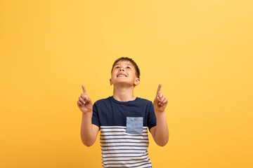 Wall Mural - Cool boy in casual t-shirt pointing up at copy space