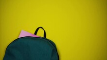 Colorful School Supplies Moving To Green Backpack On Yellow Background. Back To School Concept. Stop Motion