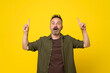 50s age excited handsome mature bristle man in green shirt, pointing upwards with finger, having great idea, isolated on yellow background. Mustach man pointing above by finger shocked with open mouth
