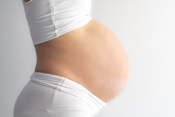 Wall Mural - Middle part of unrecognizable standing woman with very round pregnant baby bump. Side view. White background. Bright shot.