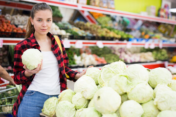 Wall Mural - Portrait of a positive customer girl in a store near the counter, holding a cabbage in her hands