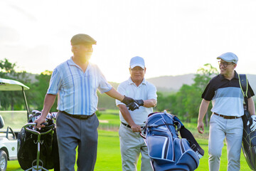 Group of Asian businessman and senior CEO holding golf bag walking on golf course with talking together. Healthy people enjoy outdoor sport lifestyle golfing at country club on summer holiday vacation