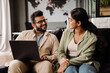 © Drobot Dean - Indian colleagues using laptop while sitting on couch in office