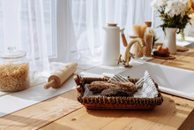 Fresh Bread And Utensils On The Kitchen Table, Ready To Be Cooked. Simple Modern Scandinavian Style Kitchen, Kitchen Details, Wooden Table, Bouquet Of Flowers In A Vase On The Table.