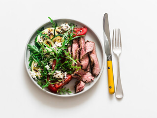 Delicious balanced lunch - steak and vegetable salad with grilled zucchini, tomatoes, arugula, feta on a light background, top view