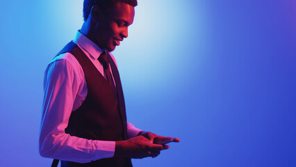 Business chat. Mobile app. Digital communication. Pink neon light smiling man texting message using phone on blue color empty space background.