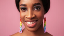 Color Makeup. Happy Face. Summer Beauty. Cheerful Smiling Woman With Full Lips Blue Eye Shadow Long Eyelashes Rainbow Earrings On Pink Free Space.