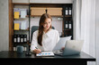 © laddawan - Young beautiful woman typing on tablet and laptop while sitting at the working wooden table office.