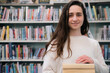 © Westend61 - Young librarian standing with books in library