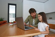 © Westend61 - Smiling girl learning to use laptop with father at home