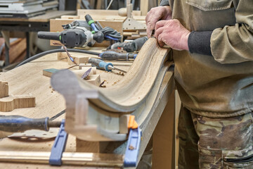 Wall Mural - Carpenter sands bending wooden railing with sandpaper in workshop closeup. Senior master makes detail of spiral staircase for home interior