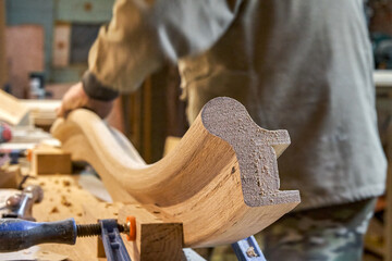 Wall Mural - Carpenter sands bending wooden railing with sandpaper in workshop closeup. Senior master makes detail of spiral staircase for home interior