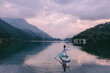 athletic woman sits on sup board. Paddle board on a beautiful lake at sunset. Sports on the water. Silence, carelessness and outdoor recreation. Beautiful sunrise landscape. Adventure in Italy Alps.