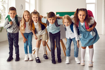 group of happy children huddling in the classroom. team of cheerful adorable friends with backpacks 