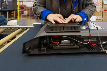 Workshop worker assembling TV on assembly line.