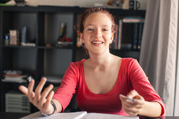 happy teen girl waving hand talking to webcam on laptop