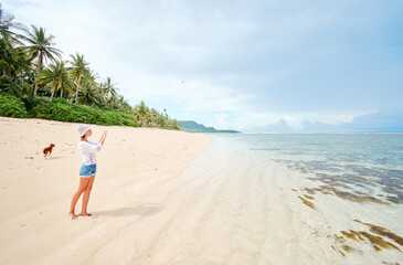Wall Mural - Vacation and technology. Young woman taking photo of beautiful tropical beach on smartphone.