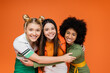 © LIGHTFIELD STUDIOS - Portrait of positive and interracial teenage girlfriends in trendy outfits hugging each other and looking at camera while standing isolated on orange, trendy generation z concept
