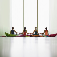 Wall Mural - Women on cushions holding hands at window in restorative yoga gym studio