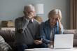 Unhappy old wife and husband sit on couch in living room with laptop and calculator manage family finances, feel desperate due debts, unpaid bills, lack of money to pay monthly bills or bank mortgage