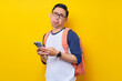 © Bangun Stock Photo - Unhappy young Asian man student in casual clothes backpack glasses standing while using mobile cell phone, chatting online isolated on yellow background. high school university college concept