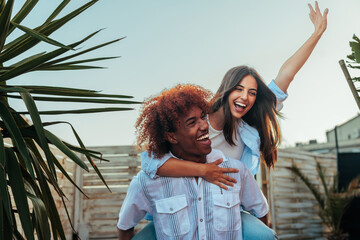 Young African-American man carrying Caucasian woman on back.