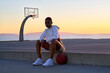 © Connect Images - Portrait of mid adult woman sitting on basketball at sunset