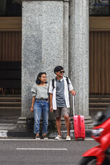 Young tourist couple standing at a road in the city waiting to cross in the middle of busy traffic