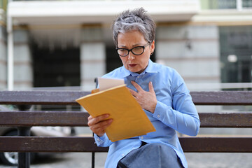 Sticker - A woman with an anxious worried look is sitting on a bench holding a large envelope with a letter in her hands.