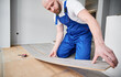 © anatoliy_gleb - Male construction worker laying laminate wooden plank on floor underlayment in living room. Man in work overalls installing laminate timber flooring in apartment under renovation.