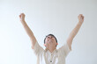 A young Asian man wearing a beige shirt is raising both hands with an excited facial expression. Isolated white background.