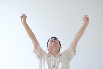 a young asian man wearing a beige shirt is raising both hands with an excited facial expression. iso