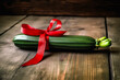 Seductive wrapped courgette with a red bow on rustic wooden table, for naughty Valentine's Day gift. Sensual and unexpected surprise, evoking playfulness in love. Generative AI