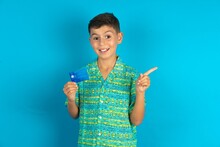Curious Smiling Little Hispanic Boy Wearing Green Aztec Shirt Showing Plastic Bank Showing Finger Copyspace