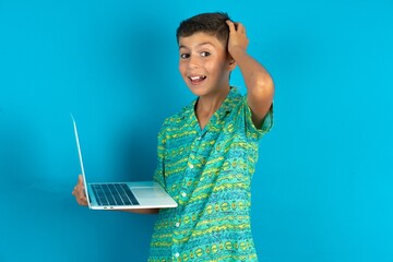 Wall Mural - Photo of amazed Little hispanic boy wearing green aztec shirt holding modern gadget arm head