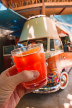 Hand Of Man Holding Orange Cocktail Drink Glass With Street Food Van Parked At The Roadside In Costa Rica