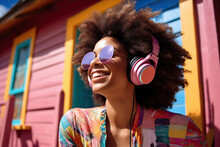 Generative AI Illustration Of Happy African American Woman With Afro Hair In Colorful Outfit, Sunglasses And Headphones Near Pink House Enjoying Sun