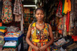 © ADDICTIVE STOCK - Generative AI image of smiling African female fabric vendor looking at camera while standing in shop with multicolored and assorted clothes for sale