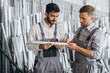 © anatoliycherkas - Two international male workers in uniform discuss the work process at a metal-plastic window factory