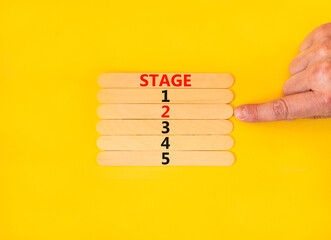 Time to stage 2 symbol. Concept word Stage 1 2 3 4 5 on wooden sticks. Businessman hand. Beautiful yellow table yellow background. Business planning and time to stage 2 concept. Copy space.