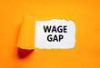 Wage gap symbol. Concept words Wage gap on beautiful white paper on a beautiful orange background. Business, support and wage gap concept. Copy space.