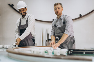 An international team, two workers work at a machine at a factory of PVC windows and doors